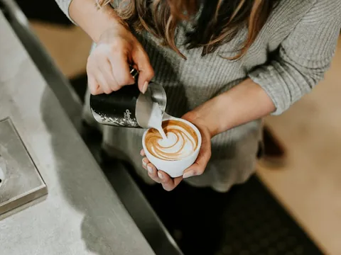 Hands pouring milk into a latte.